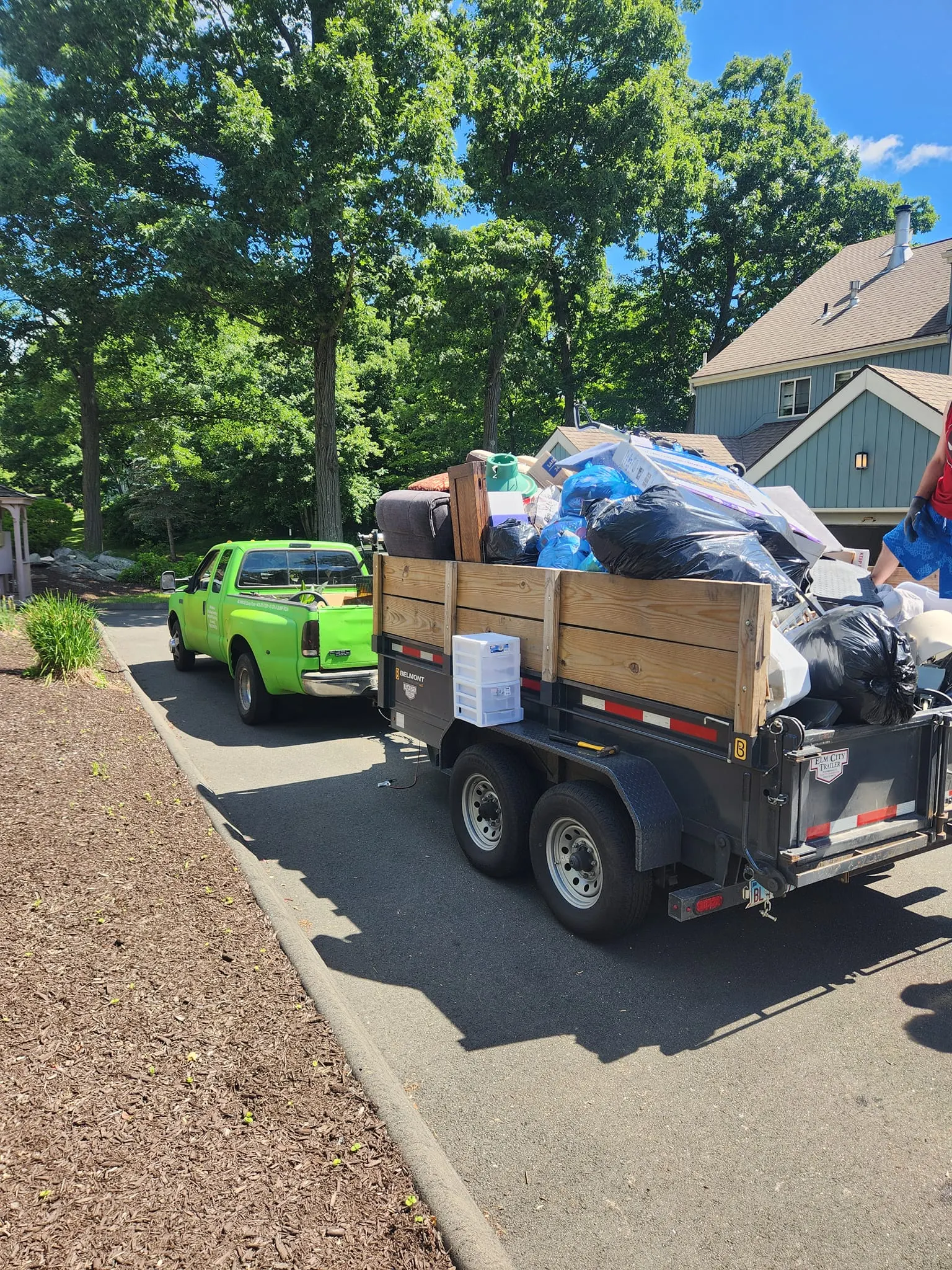 Green pickup truck and trailer loaded after a cleanout in a Shelton driveway